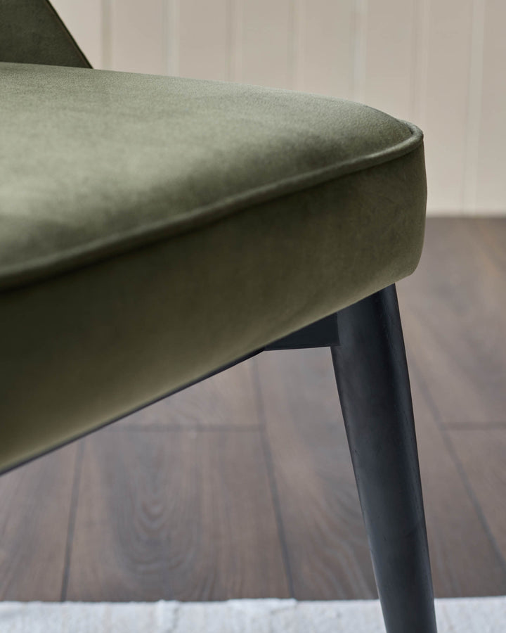 Close-up of an olive green chair with dark wooden legs and a plush seat, showcasing its stylish design.