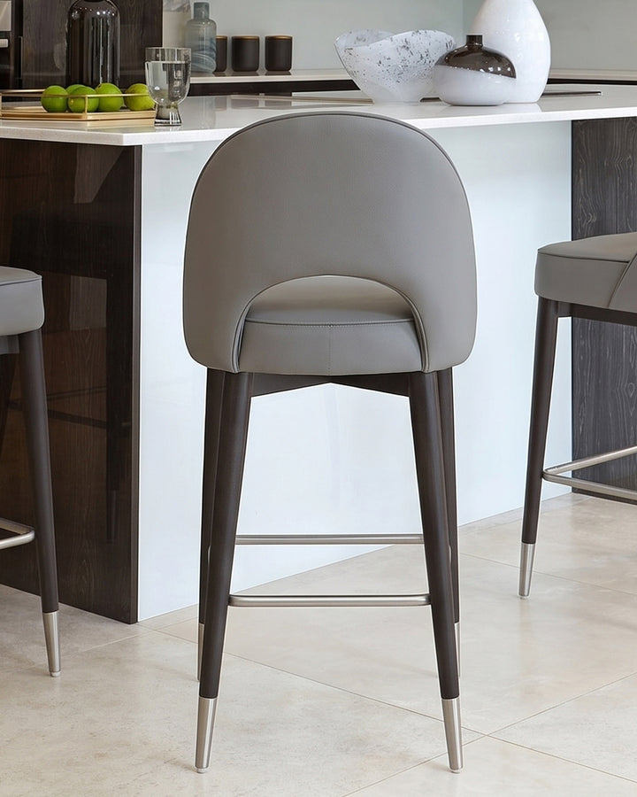 Clover faux-leather bar stool in mid-grey with dark wood legs and metal feet detail, shown at a kitchen island.