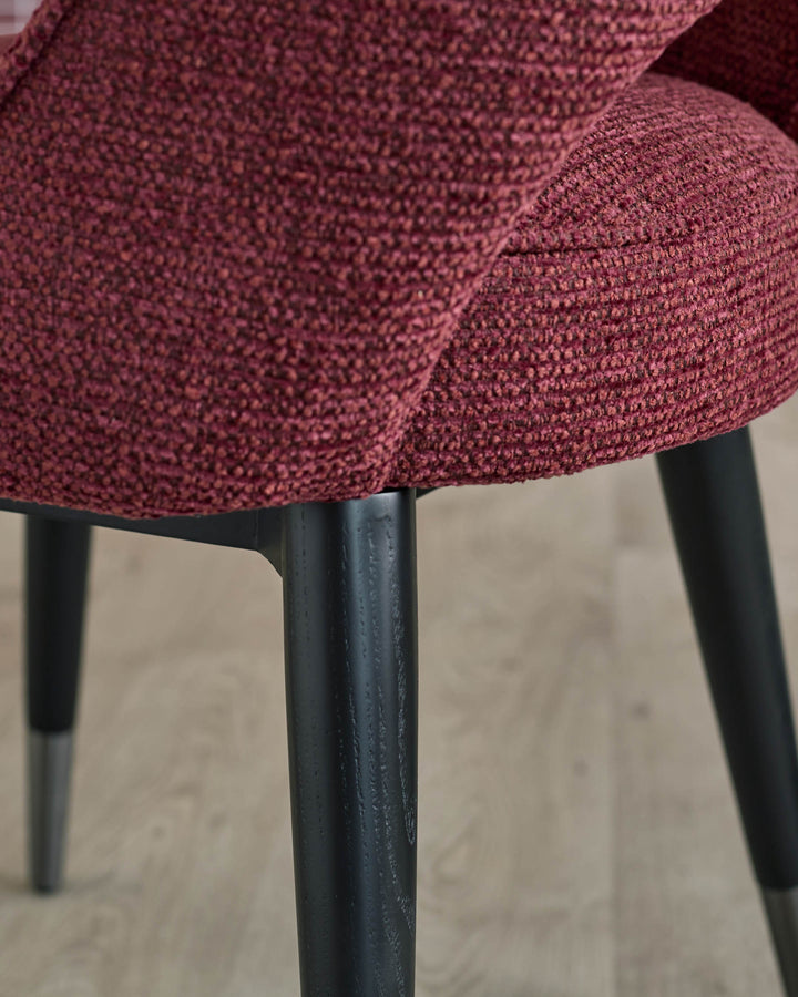 Close-up of a stylish red upholstered chair with sleek black legs, showcasing its modern design.