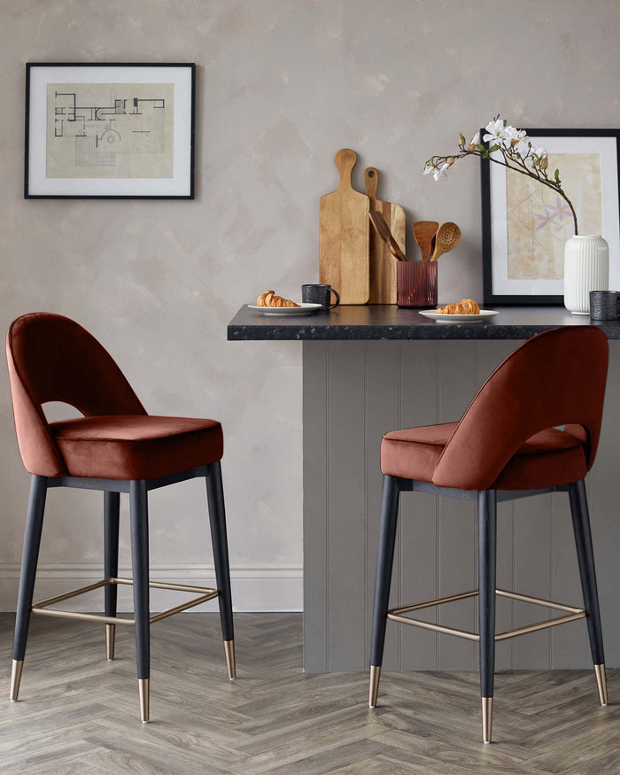 Two stylish rust-coloured velvet bar stools with sleek black legs and gold accents sit at a kitchen island.