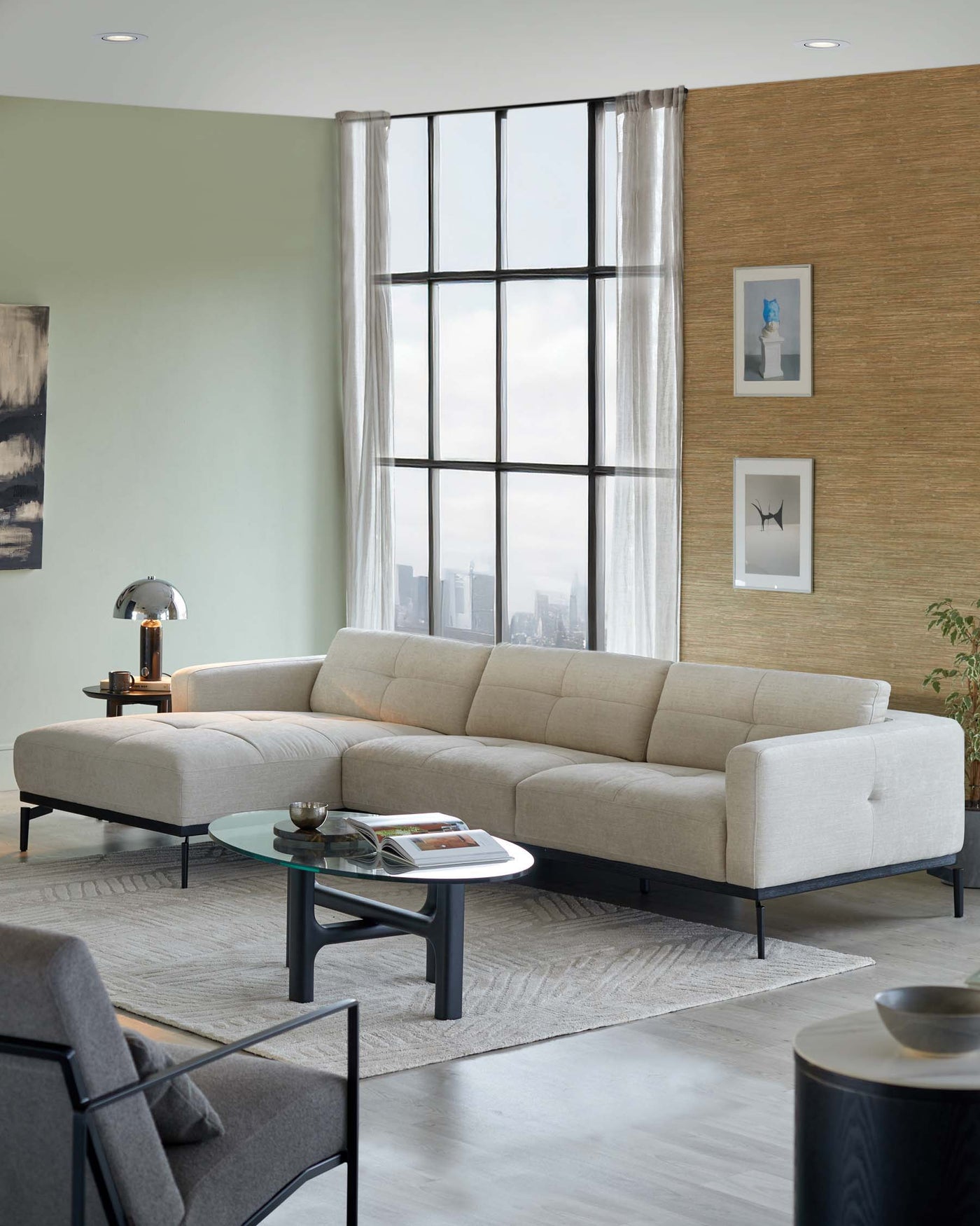 Modern sectional sofa in light beige with a minimalist design and dark tapered legs, paired with a round glass-top coffee table featuring a unique blue and black base, on a light grey area rug.