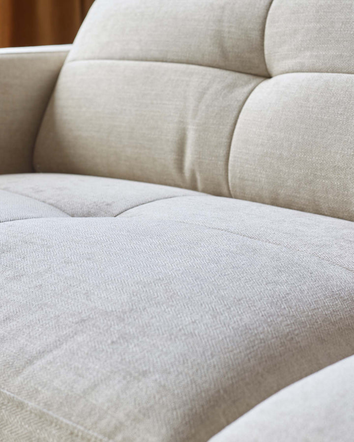 Close up of a cream sofa with textured fabric and button detailing on the back and seat cushions.
