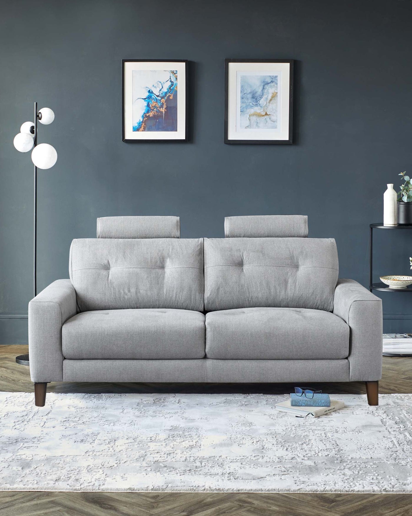 Modern three-seater sofa with a minimalist design, featuring a smooth, grey upholstery and button-tufted back cushions. The sofa stands on four round, tapered wooden legs, presented on a textured white area rug against a dark wall, creating a contrast that highlights the couch's sleek lines and contemporary aesthetic.