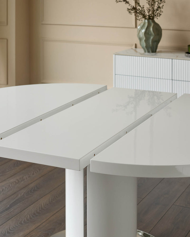 White gloss round extending dining table with leaf extension partially opened, showing the extension mechanism and sleek cylindrical pedestal base.