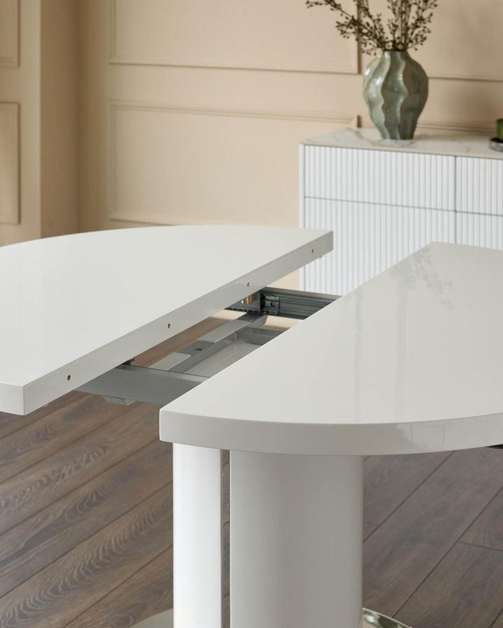 Curva white gloss round extending dining table with extension leaf pulled open, showing internal mechanism on wooden floor.