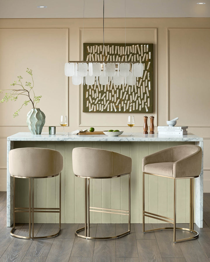 Dakota velvet barstool in champagne with brass frame, shown in kitchen setting at marble counter.
