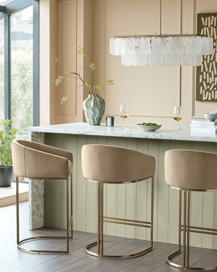 Dakota velvet barstool in champagne with brass frame, shown at marble countertop in modern kitchen setting.