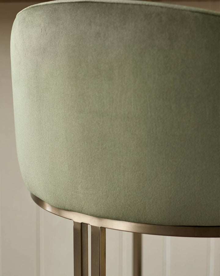 Dakota bar stool in olive green velvet with brushed metal base and footrest detail, close-up side view.