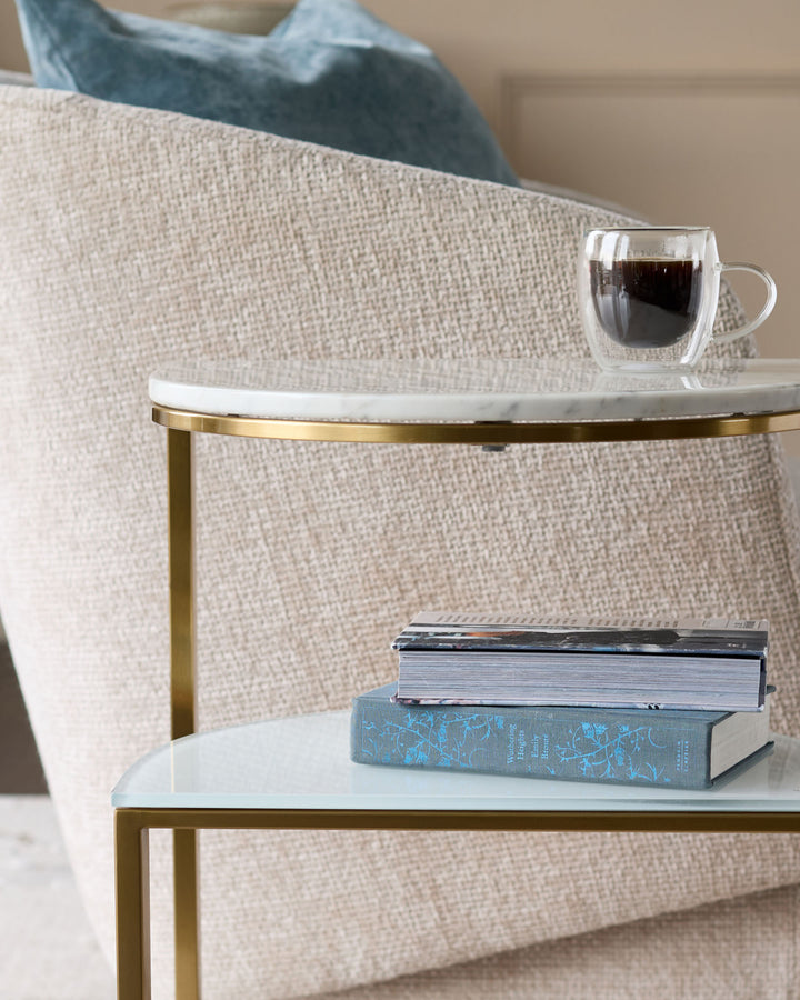 White marble demi-side table with brass frame, styled with books and a coffee cup.
