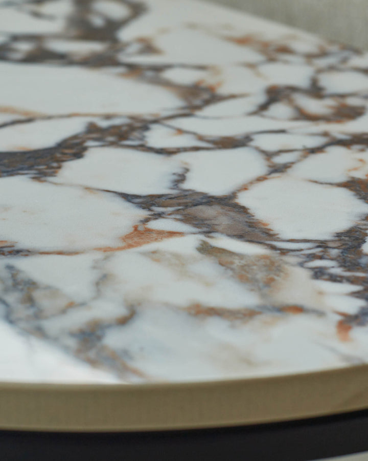 Close-up of a round marble table top with brown and grey veining and a gold edge.