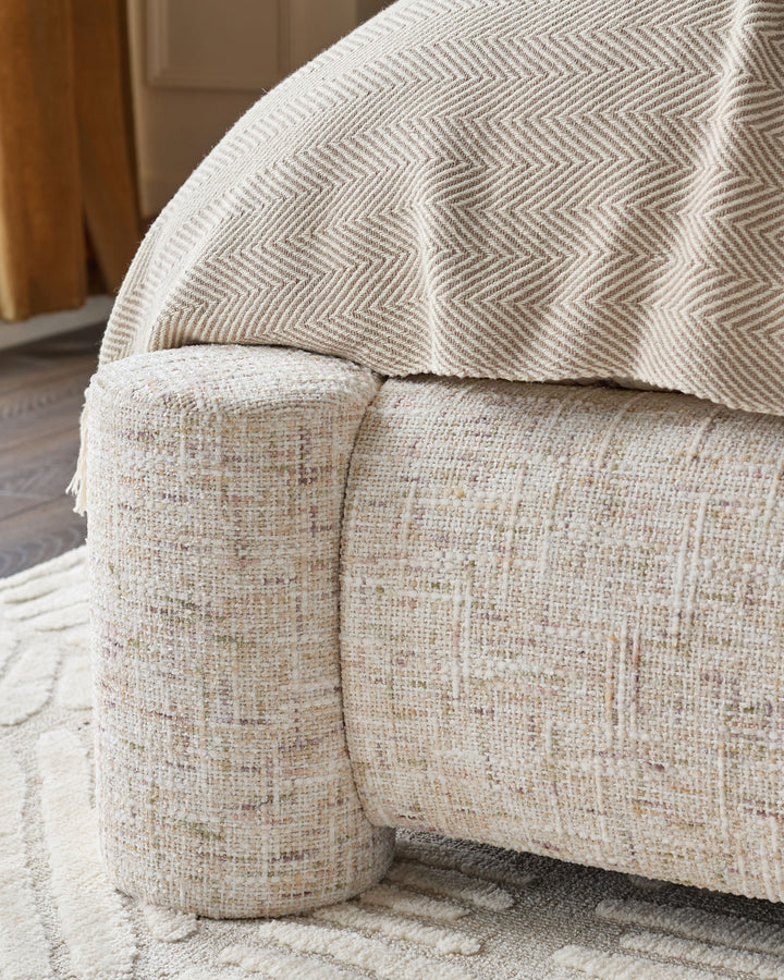 Deven king-size ottoman bed in natural fabric, close-up of curved cylindrical foot detail and herringbone pattern cushion.