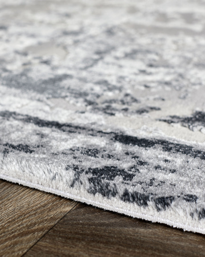 Distressed border textured rug in grey and white tones, close-up showing pile detail on wooden floor.