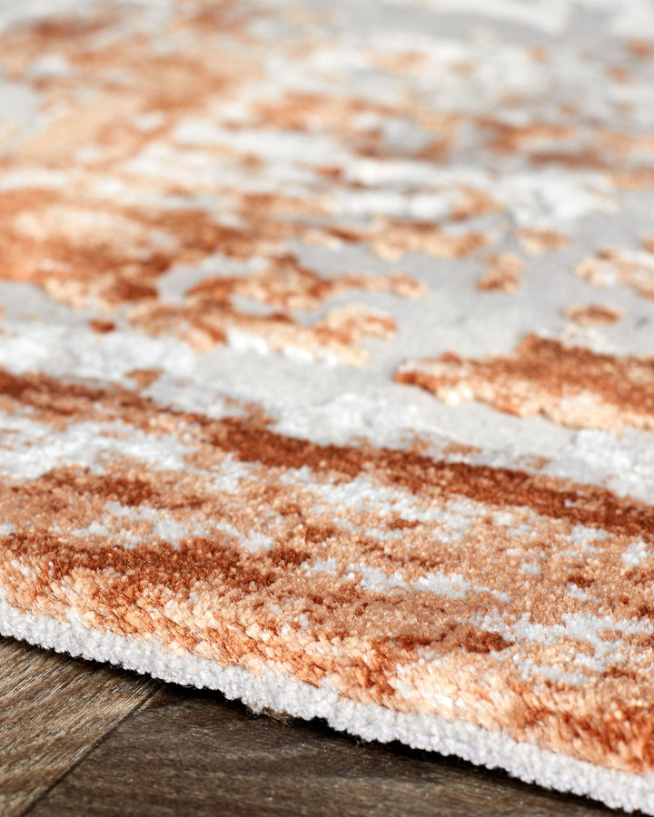 Distressed border rust textured rug with white accents, displayed at an angle on wood flooring.