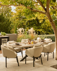 Donato dining table with six Camilo chairs in cream upholstery and dark grey legs, set on a terrace under a tree.