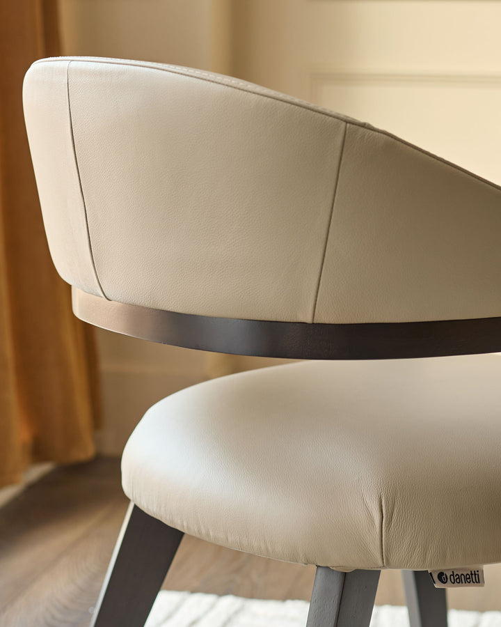 Dylan Dining Chair in natural leather, side angle view showing curved backrest and dark wood legs with Danetti branding.