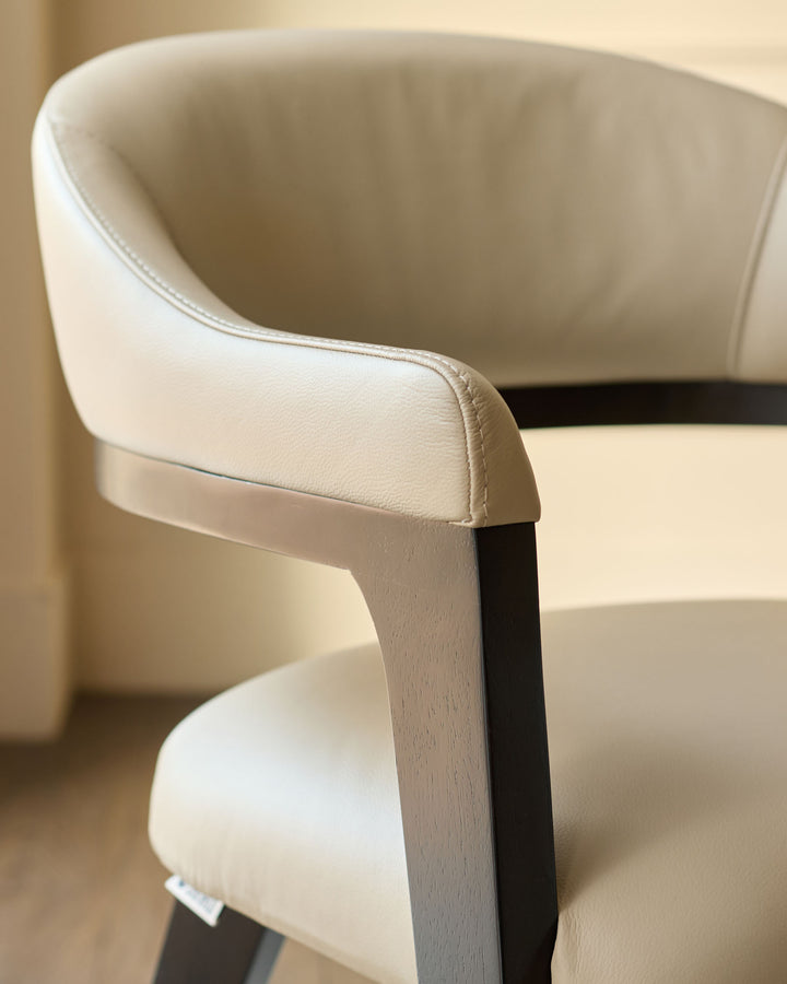 Dylan dining chair in natural leather, side angle view showing curved backrest and dark wooden frame detail.