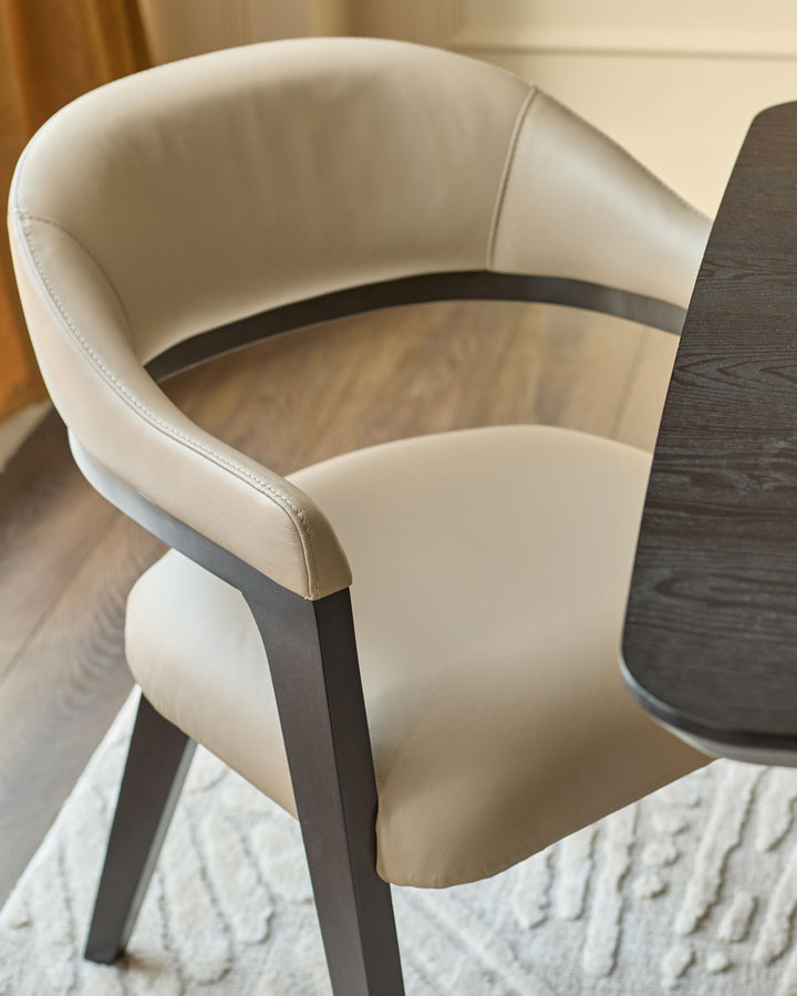Dylan dining chair in natural leather with dark wood frame, shown from side angle at table.