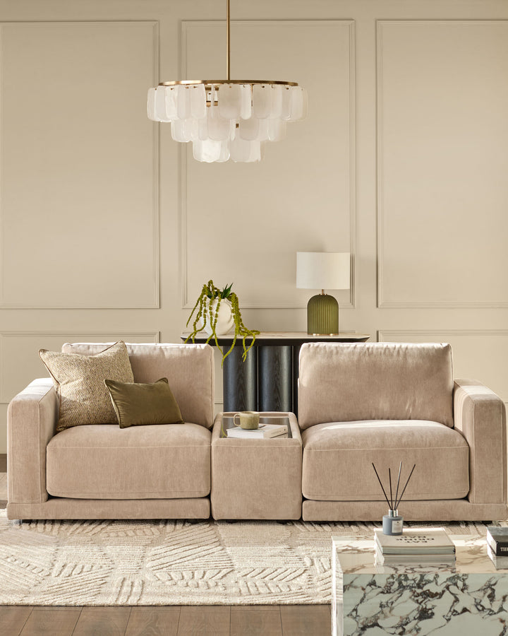 Champagne fabric side table module with glass top, shown between two beige sofas in a neutral living room setting.
