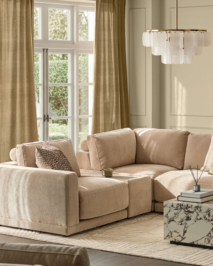 Eden side table module in champagne fabric with glass top, shown in living room setting with beige sectional sofa.