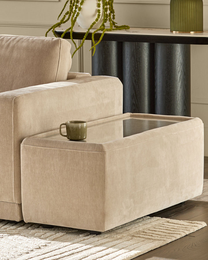 Champagne fabric side table with open glass-top compartment, shown in living room setting next to beige sofa.