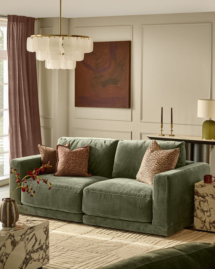 Eden 2-seater sofa in dark green fabric, shown in a styled living room setting with patterned throw pillows.