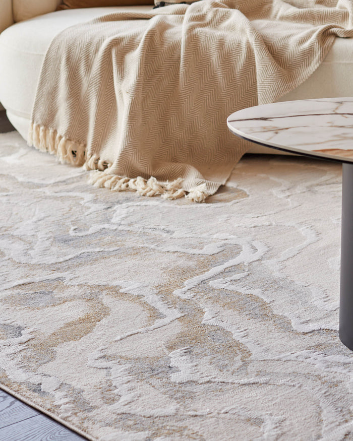 A modern living room setup with a neutral-toned patterned rug, a round couch and a marble-topped coffee table.