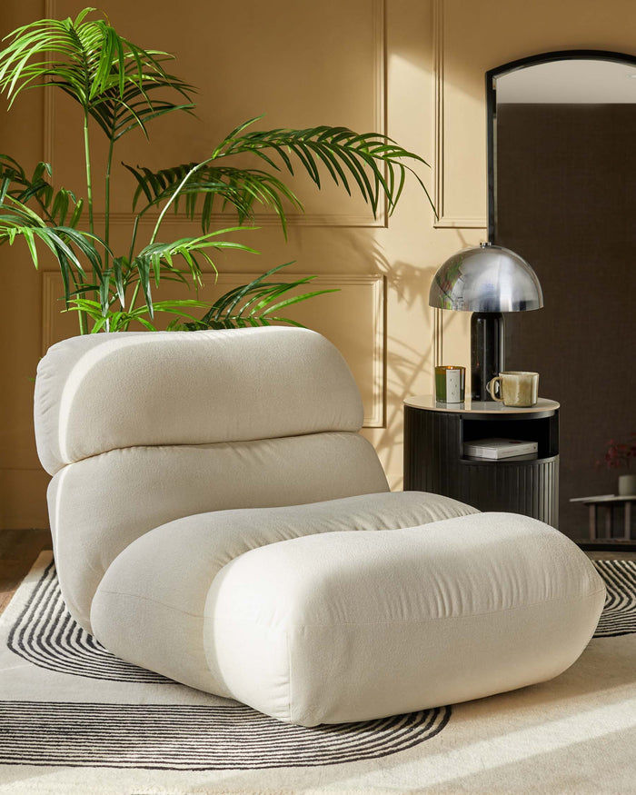 A cosy, cream-coloured modular sofa chair on a patterned rug, beside a stylish side table with a lamp and decorative items.