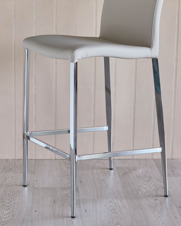 A chrome stool with a padded cream seat against a panelled wall and light wood floor.