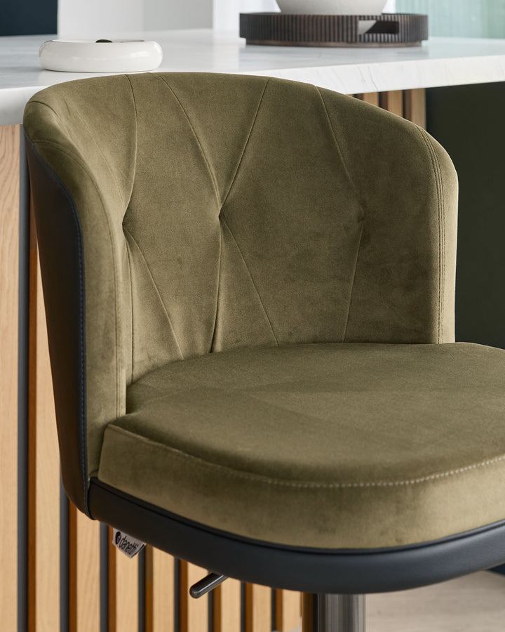 Olive green velvet bar stool with quilted backrest and black metal base, shown at an angle in a modern interior setting.
