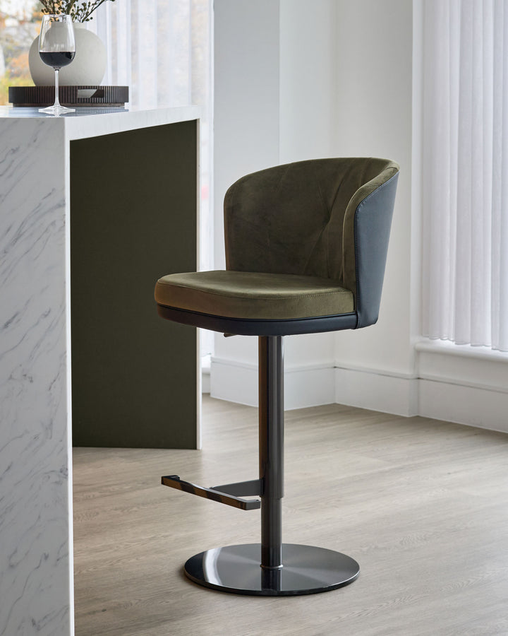 Elodie gas lift bar stool in olive green velvet and black faux leather with black metal base, shown in modern interior setting.