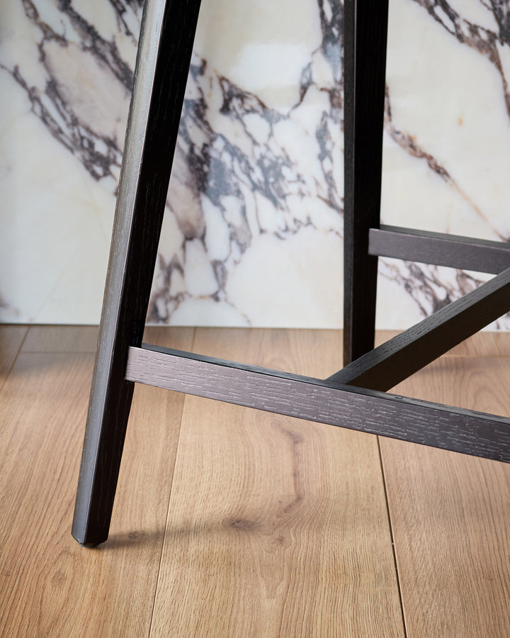 Dark grey bar stool with black metal frame, shown from a low angle on wooden flooring with marble backsplash.