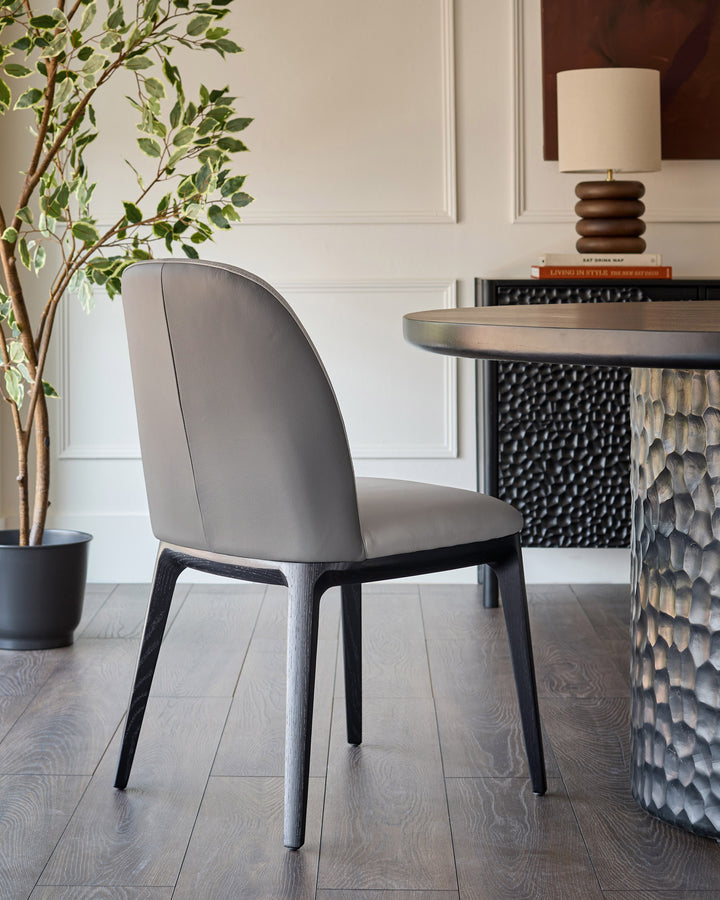 Emerson dining chair in light grey leather with dark grey wood legs, shown in a styled interior setting.