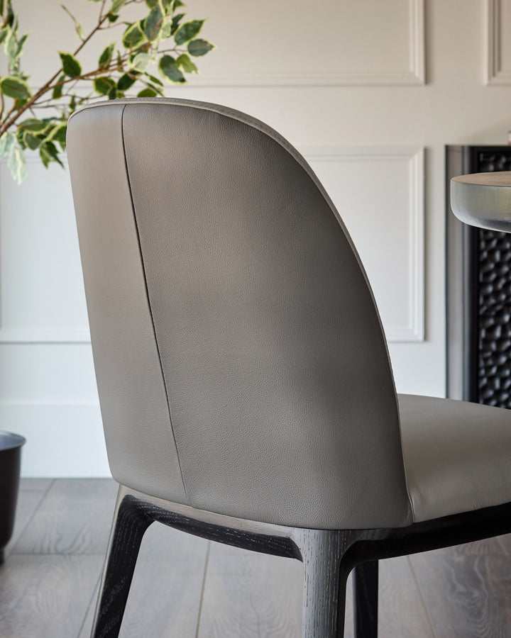 Emerson dining chair in light grey leather, shown from back angle with dark grey wooden legs.