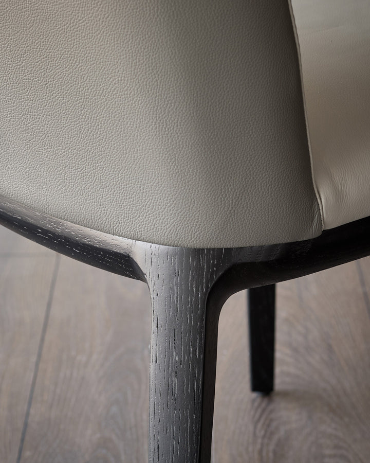 Emerson dining chair detail showing light grey leather seat and dark grey wooden frame legs.