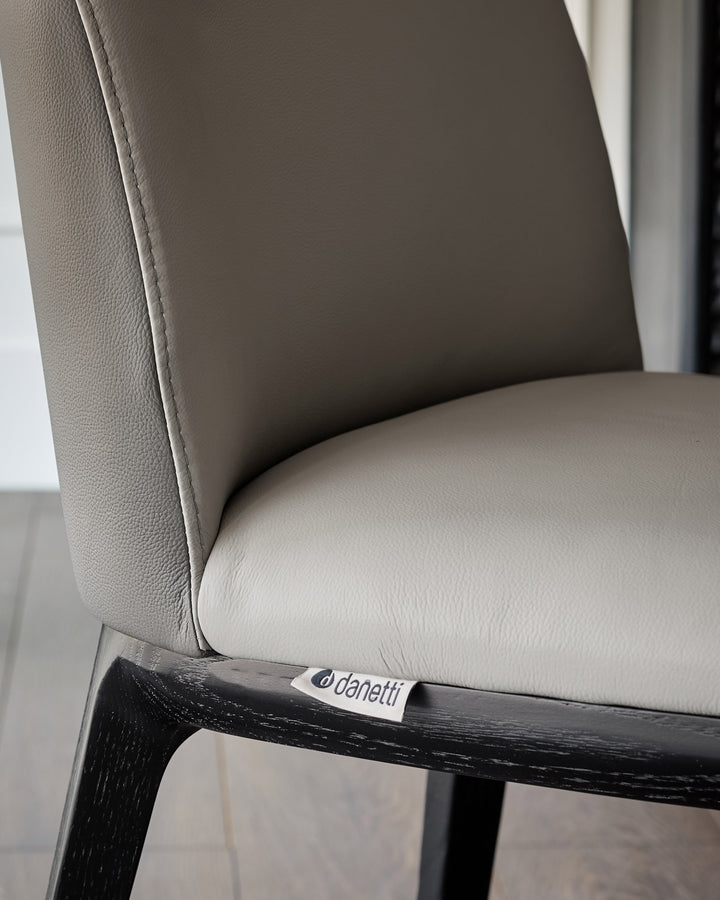 Emerson dining chair in light grey leather with dark grey accents, featuring a black wood frame, close-up side view.