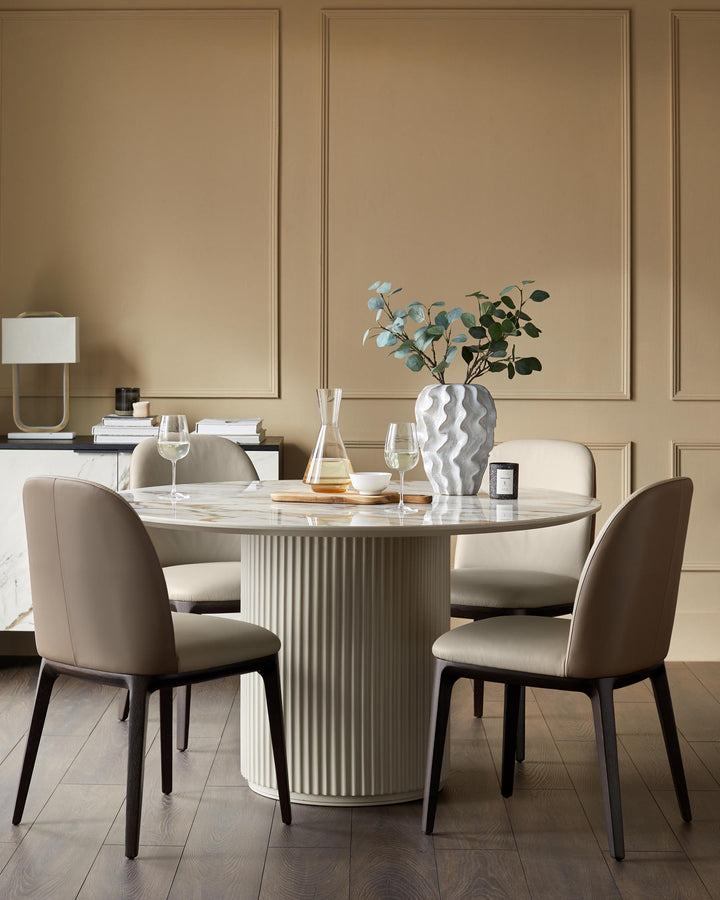 A round marble dining table with four neutral-toned chairs. A modern, minimalist design for a contemporary dining space.