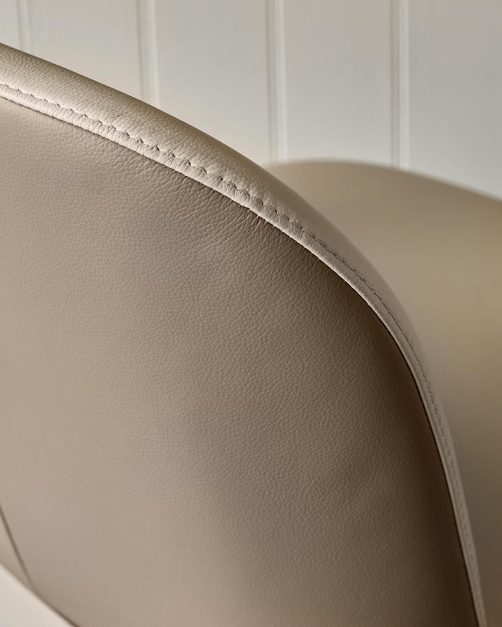 Close-up of a beige leather chair, showing the texture and stitching detail.