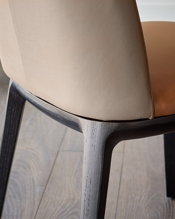 Emerson dining chair in tan leather with dark wood frame, shown in close-up detail of backrest and leg construction.