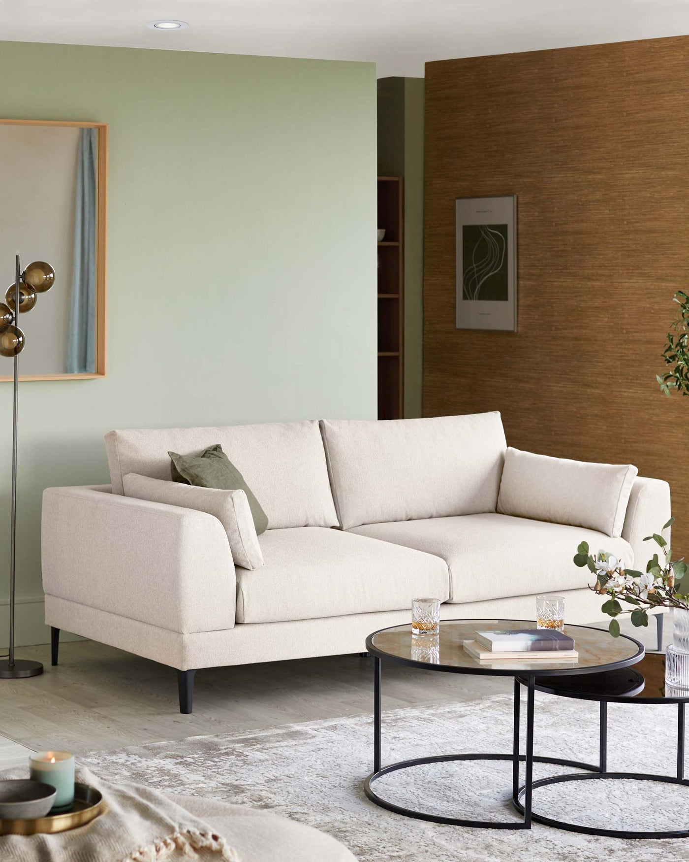 Elegant light beige corner sectional sofa with a minimalist design on low-profile black legs. Accompanied by a two-tiered round coffee table with a black metal frame and glass tops.