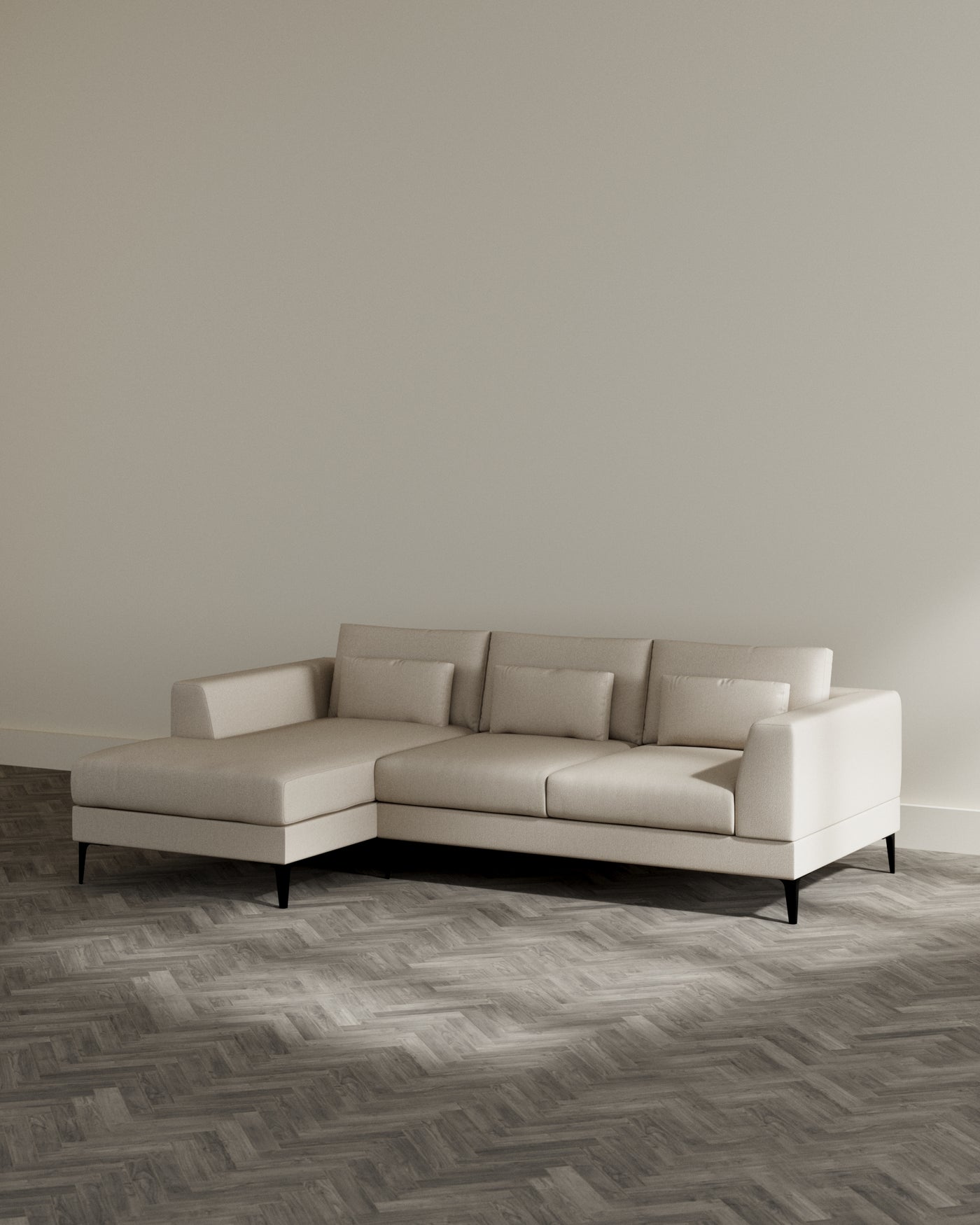 Modern L-shaped sectional sofa with a light beige fabric upholstery and sleek black legs, displayed in a minimalist setting with a herringbone patterned wooden floor.