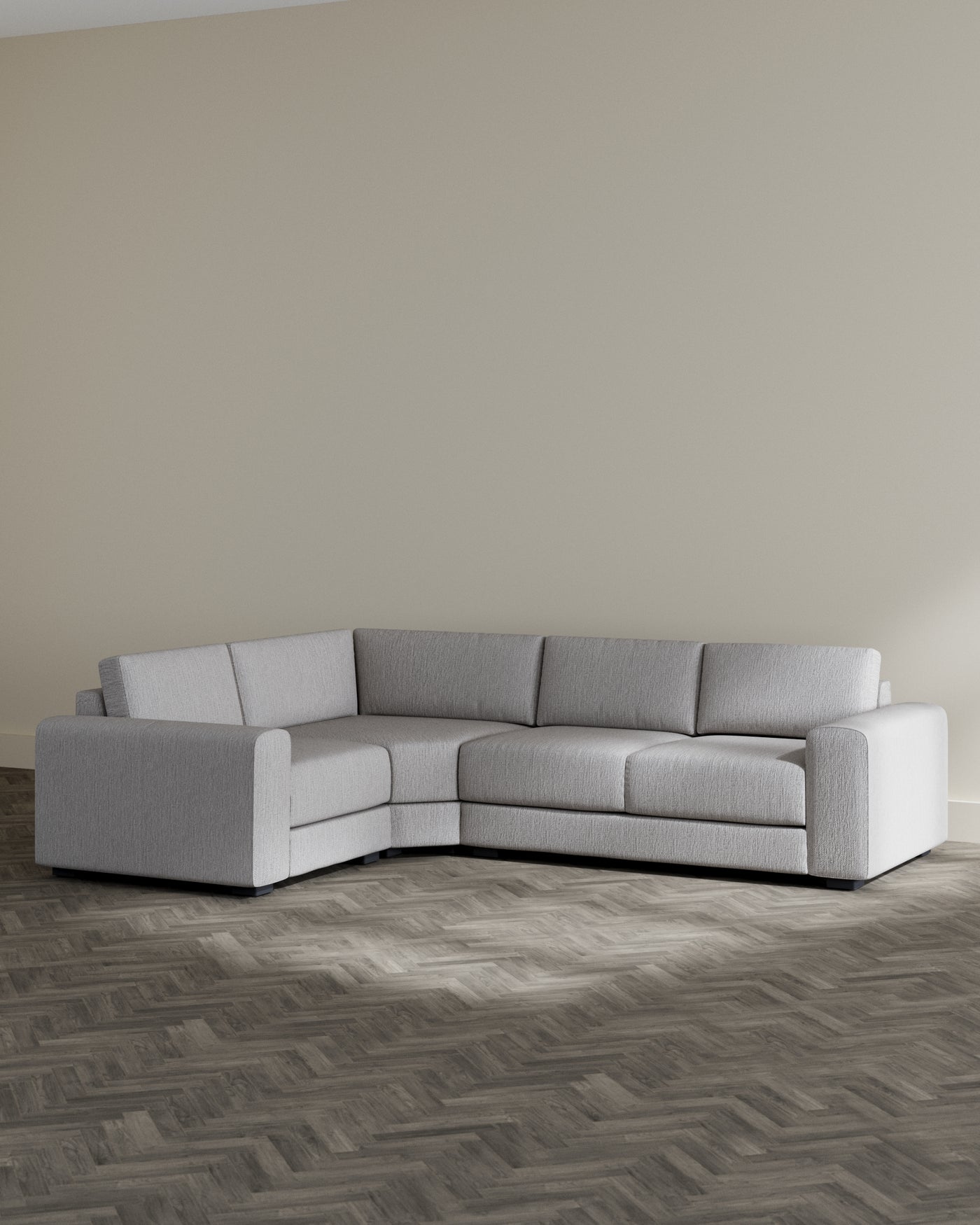Modern light grey sectional sofa with a plush texture and a simple, contemporary design. Features clean lines, wide armrests, and a modular form that can be arranged to suit various living spaces. Set against a neutral-toned wall on a dark herringbone-patterned floor.