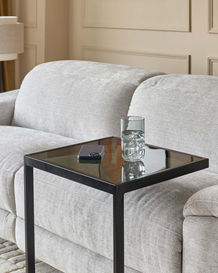 Ezra tray table with smoked glass top and black metal frame, styled next to a cream upholstered sofa.