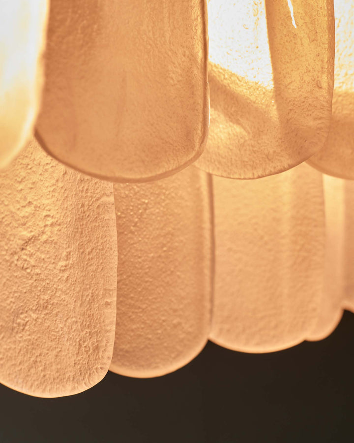 Close-up of a stylish light fixture with layered, textured panels in a warm, amber hue, suspended against a dark backdrop.