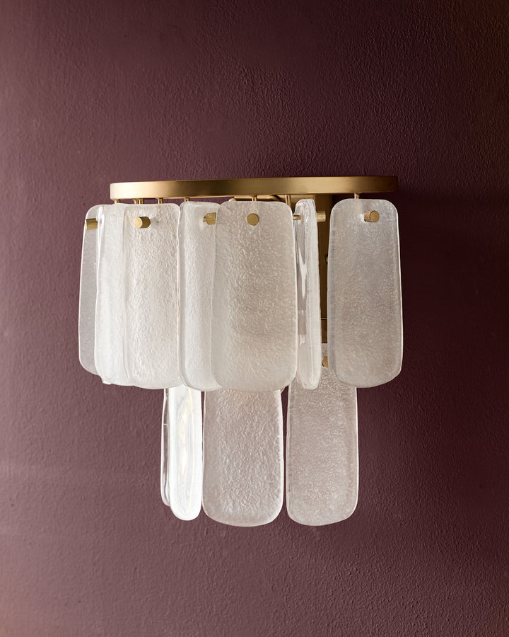 Estelle wall light with brass fixture and stacked white textured glass panels against burgundy wall.