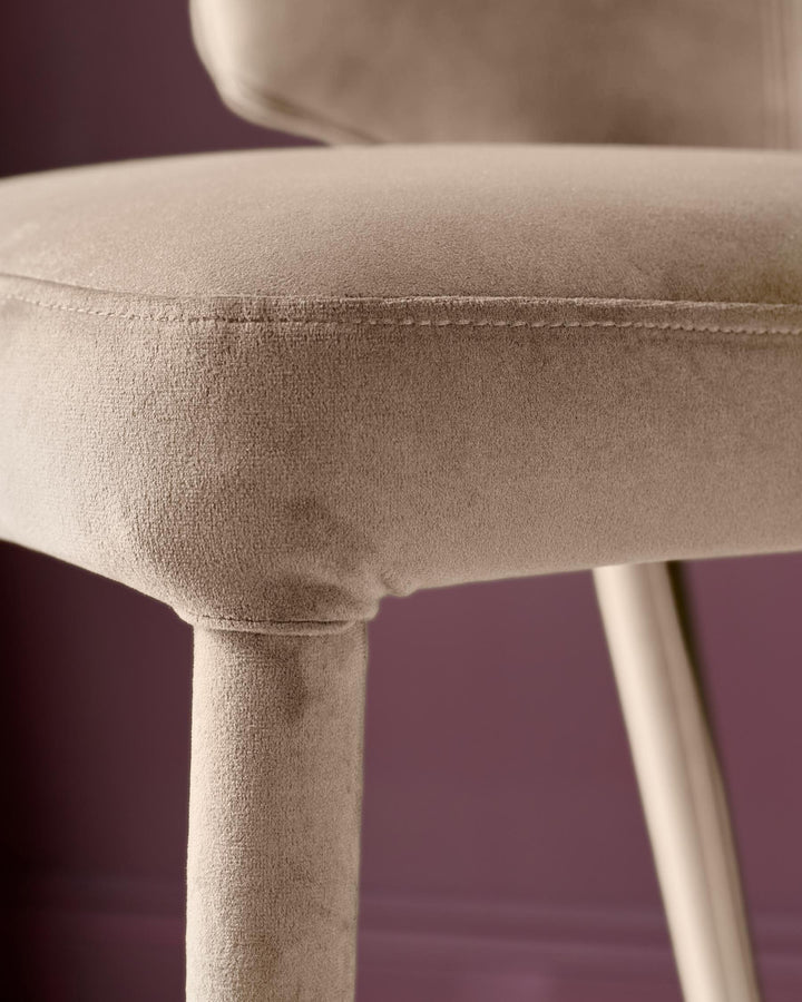 Ethan bar stool in champagne velvet, showing close-up of seat seam and wooden leg detail against purple background.
