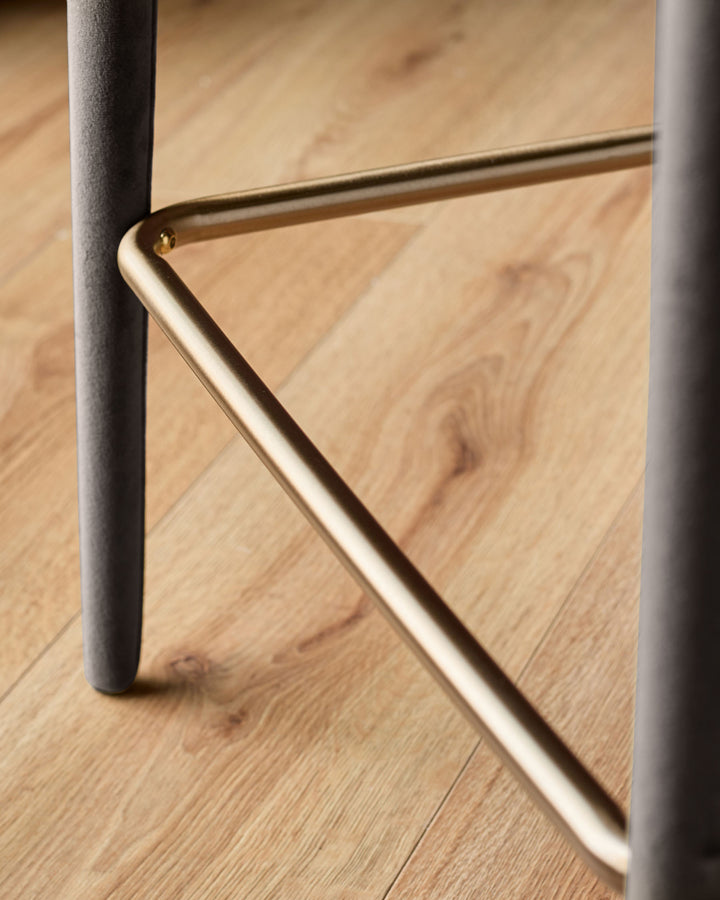 Ethan bar stool detail: brass footrest and Grey upholstered leg on wooden floor.