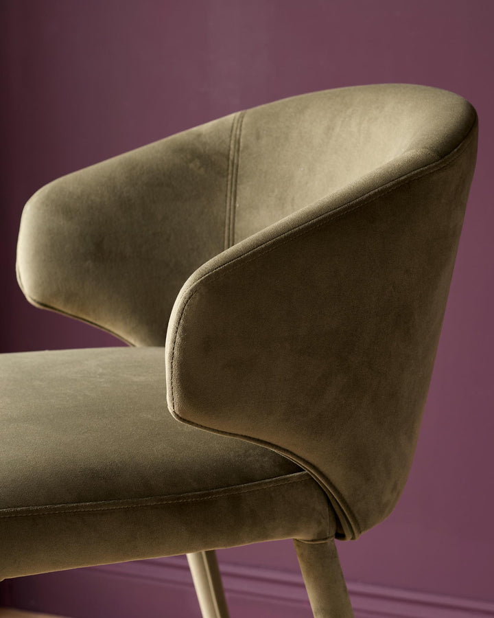 Ethan bar stool in olive green velvet, shown from side angle highlighting curved backrest and upholstered seat against purple background.