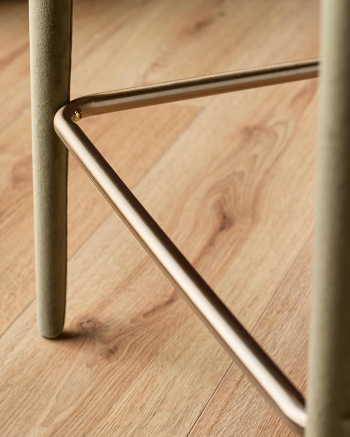 Ethan bar stool in olive green velvet with brushed metal footrest and leg detail on wooden floor.