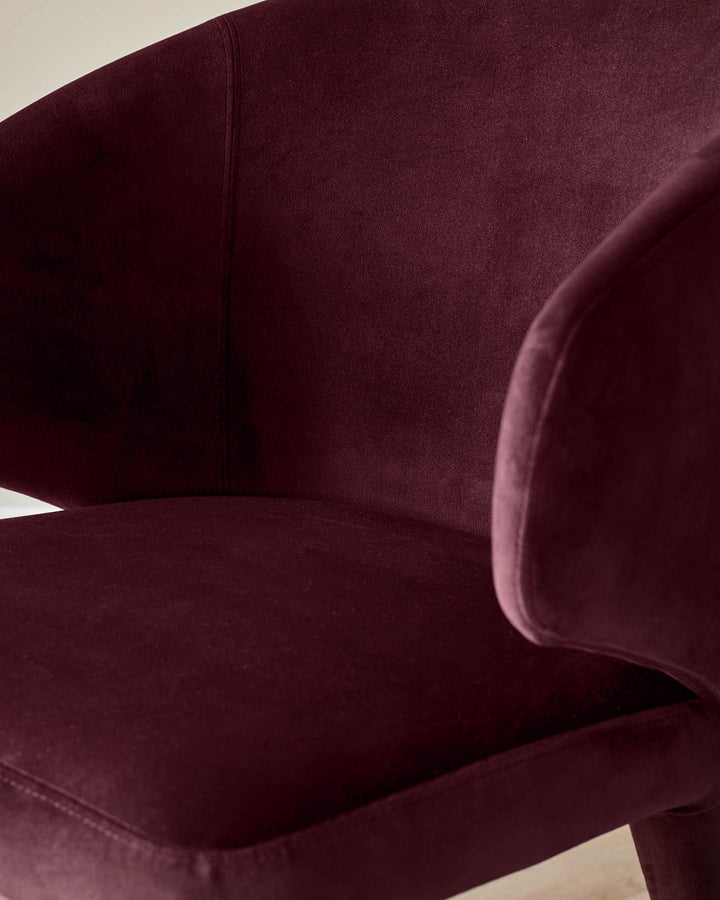 Ethan dining chair in plum velvet, shown at an angle highlighting its curved backrest and soft upholstered seat.