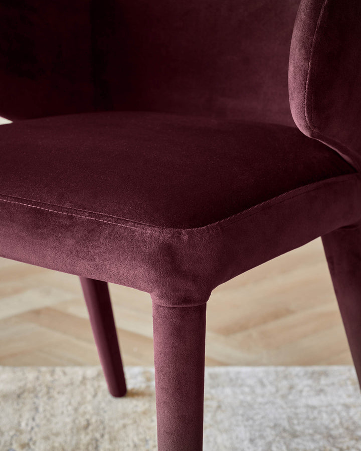 Plum velvet dining chair shown from side angle, displaying curved seat, stitched seam detail, and tapered leg on neutral rug.